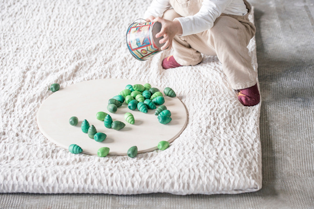 Child pouring tree mandala pieces on round wooden board