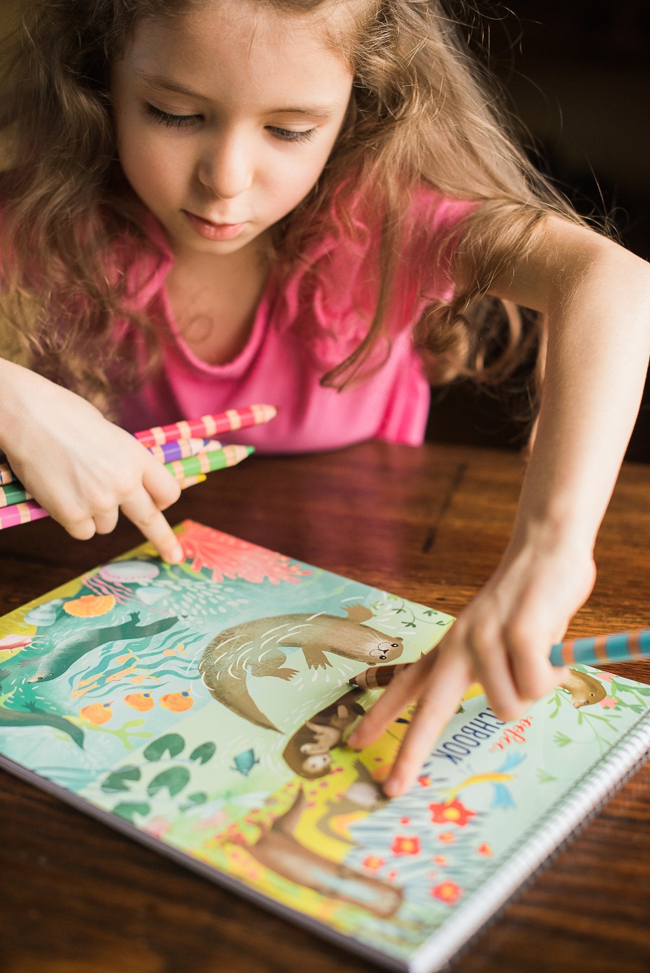 child wearing a pink shirt sitting at a table with an otters sketchbook