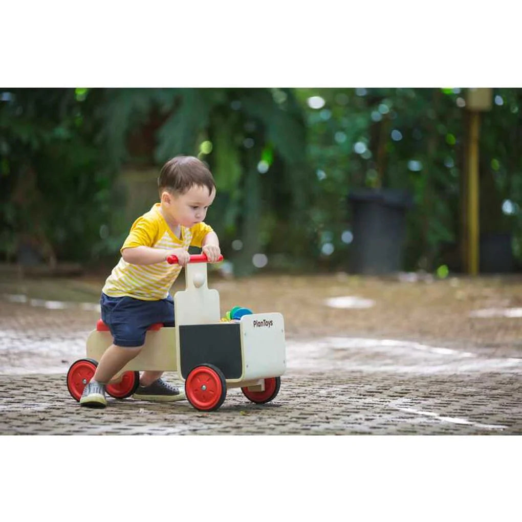 cute child riding the plan toys delivery bike over grey bricks