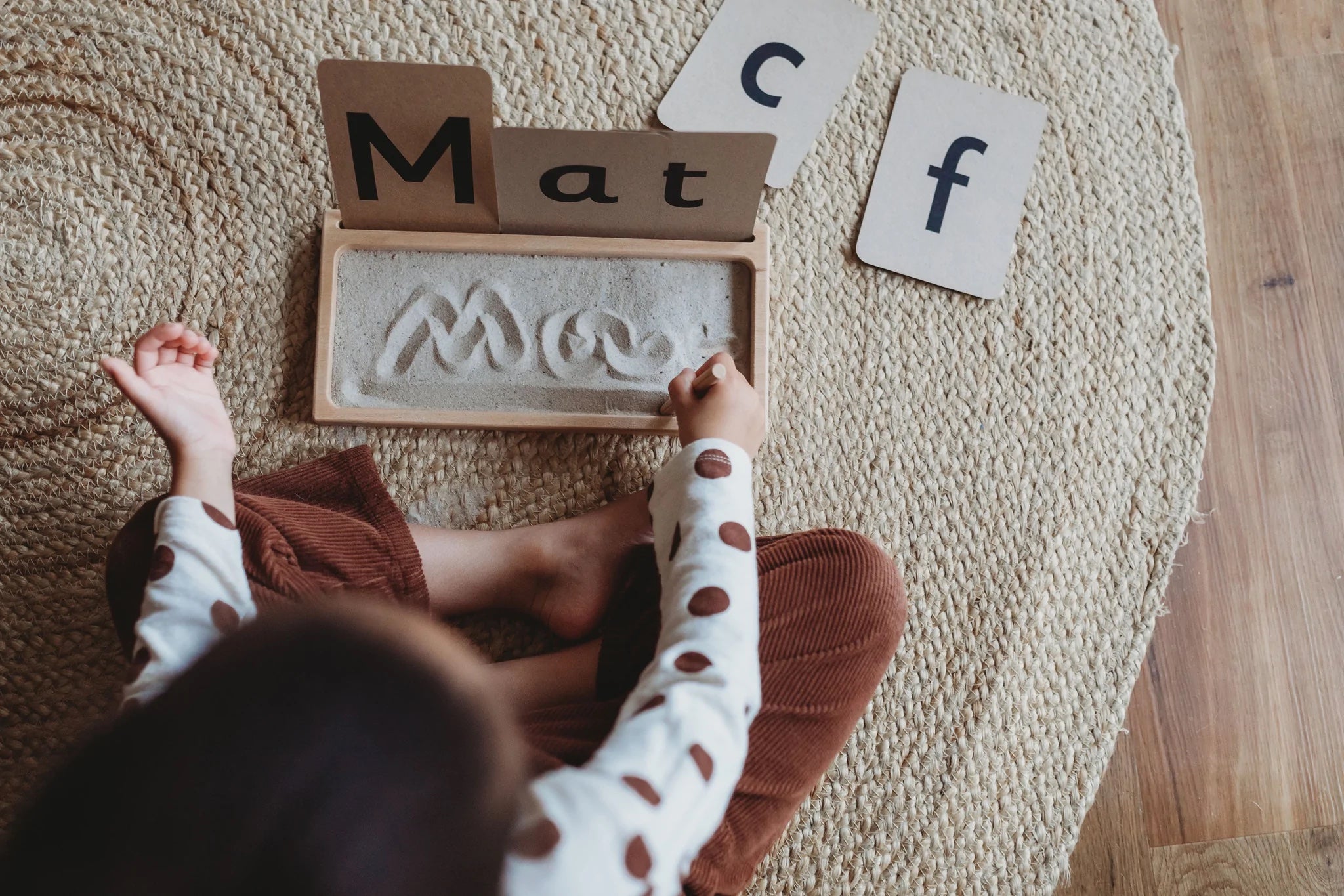 Kid writing the word "mat" on a Sand Writing Tray